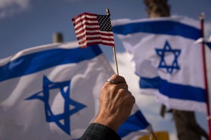 a person holds an American flag in front of Israeli flags