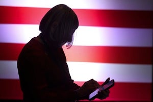 a person looks at their phone in front of an American flag backdrop
