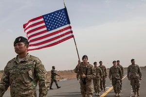 A flag bearer holds the American flag as American forces march down a road