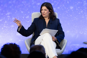 Leslie Vinjamuri talking to an audience in white pants, navy blazer