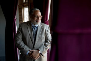 Photo of Lonnie Bunch looking out a window next to burgundy curtains