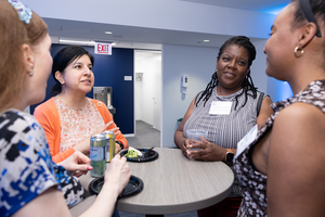 Event reception attendees standing in conversation around a table with food and drinks.