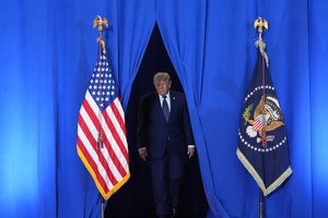 President Donald Trump walks through blue curtains
