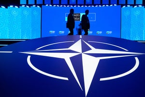 Two men walk past the NATO logo