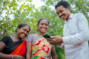 Three people stand together laughing while one holds a mobile phone