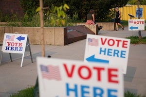"Vote Here" signs lining a sidewalk outside a voting location.