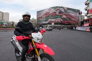 A man drives his motorbike past a huge banner showing hands firmly holding Iranian flags as a sign of patriotism, as one of them flashes the victory sign, in Tehran, Iran, Wednesday, Jan. 14, 2026. 