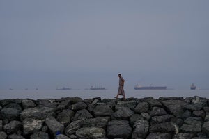 A man walks along the shore as oil tankers and cargo ships line up in the Strait of Hormuz, as seen from Khor Fakkan, United Arab Emirates, Wednesday, March 11, 2026. 