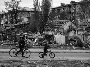 Two people ride bikes through a destroyed neighborhood in Ukraine