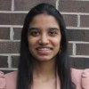 Avani Rai is pictured from the shoulders up wearing a pink blazer over a white shirt, smiling into the camera.