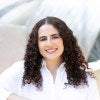 Rachel Abrams in a white professional button down shirt is smiling looking into the camera outside at Millennium Park