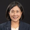 Headshot of Katherine Tai wearing black blazer, white shirt, smiling in front of dark background