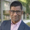 Headshot of Aziz Huq in grey jacket, pink shirt, and glasses