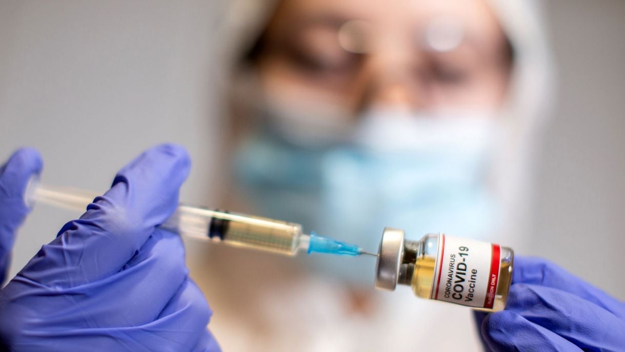 A woman holds a small bottle labeled with a "Coronavirus COVID-19 Vaccine" sticker and a medical syringe in this illustration