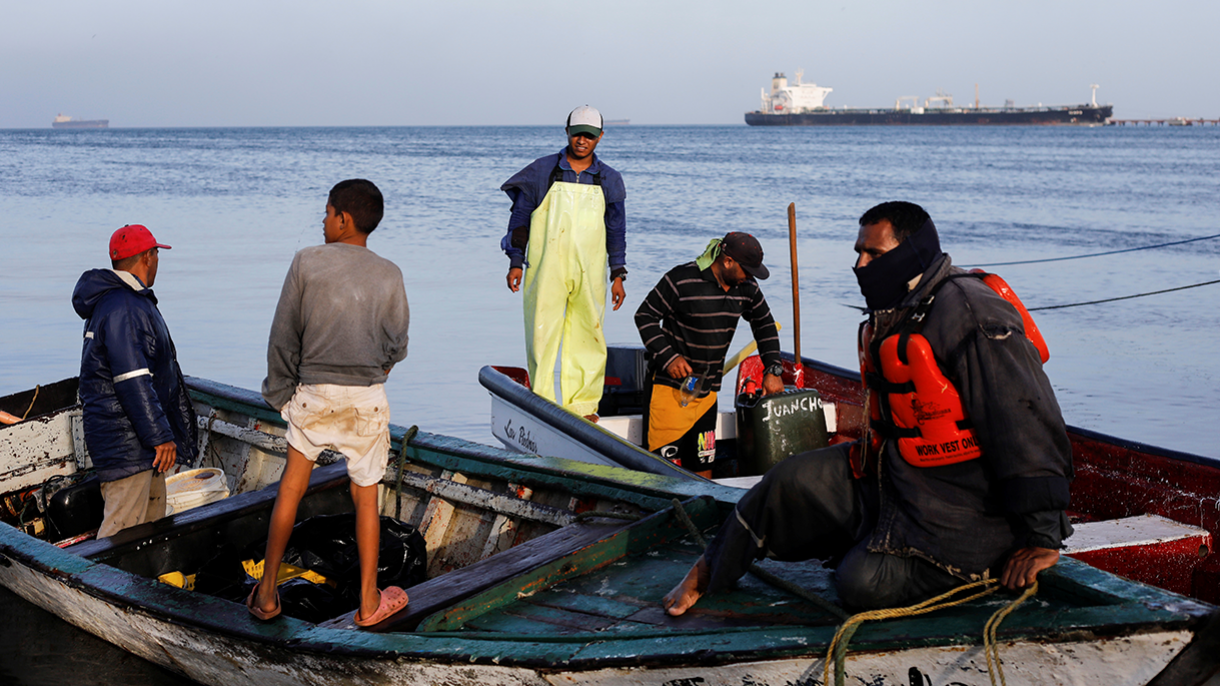 Venezuelan fisherman clean equipment from oil spill.