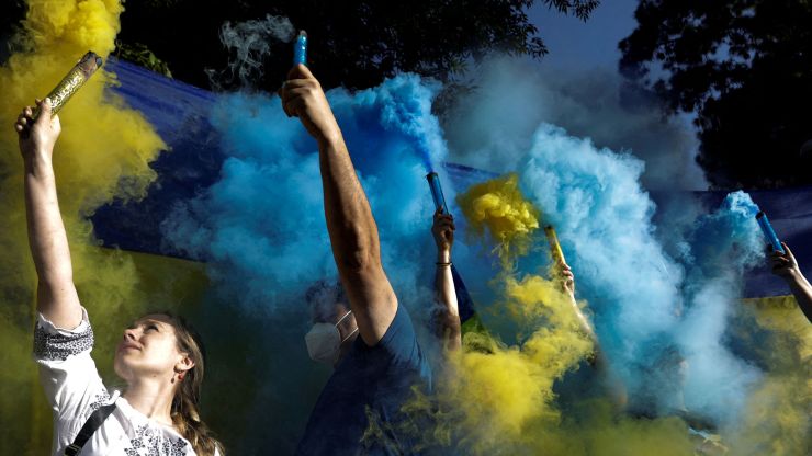 People hold flares surrounded by blue and yellow smoke