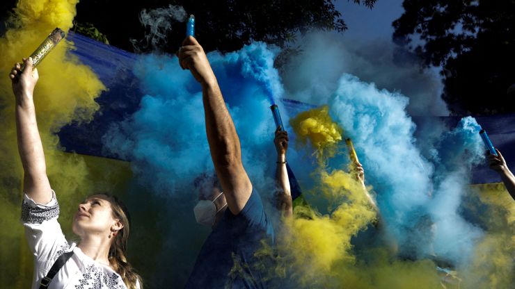 People hold flares with the colors of the Ukrainian flag at a protest against the Russian invasion.