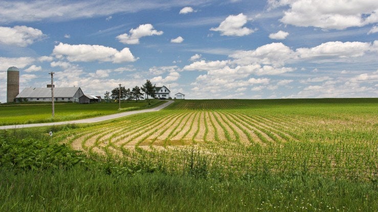 A farm building and house are pictured next to a large field.