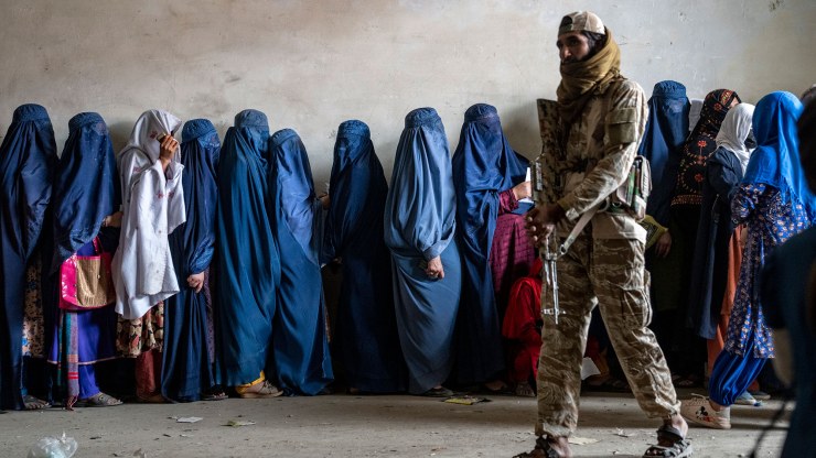 A Taliban fighter stands guard as women wait to receive food rations distributed by a humanitarian aid group in Kabul, Afghanistan.