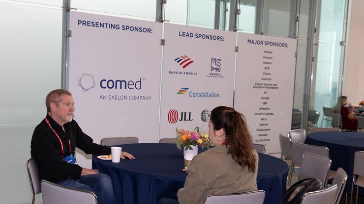 Attendees at a Council event sitting at a table in front of corporate sponsorship signage.