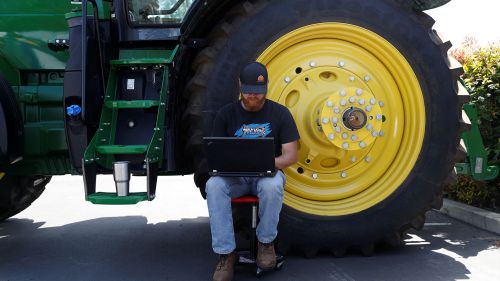 A mechanical engineer with Blue River Technology works on his computer next to a tractor.