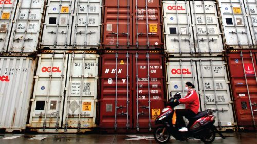 A person rides a scooter past shipping containers in the Port of Shanghai