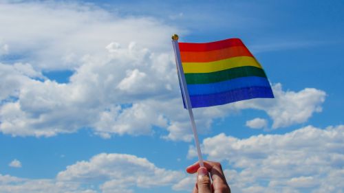 A person hold a gay pride flag against a blue sky