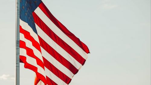 An American flag waving in wind, across a hazy sky