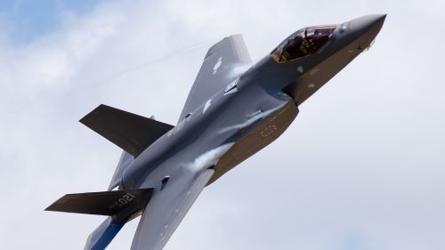 A close-up image of a military plane in the air with clouds.
