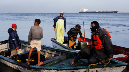 Venezuelan fisherman clean equipment from oil spill.
