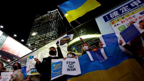 Japanese people protest Russian invasion at night near a skyscraper.