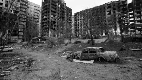 Black and white photo of a destroyed car and apartment buildings in Ukraine