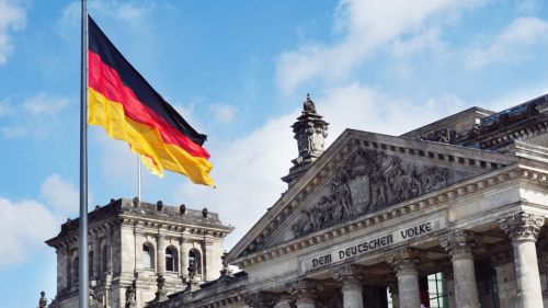German flag above a neoclassical building with the inscription "dem deutschen volke" and a blue sky.