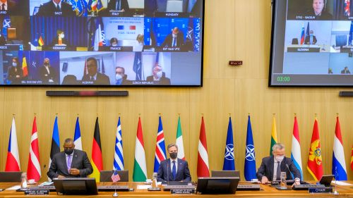 Flags on a desk below a screen showing US leaders in an online defense council meeting.