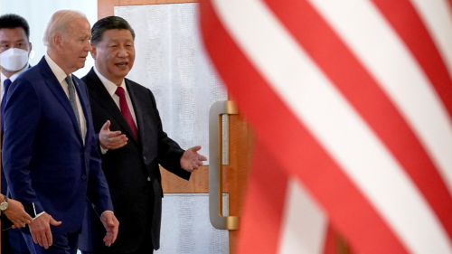 Presidents Biden and Xi talk side by side with an American flag in the foreground