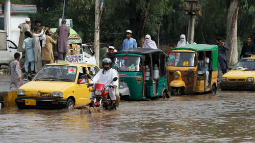 Vehicles are seen attempting to drive through a flooded street after heavy rainfall in Peshawar, Pakistan.