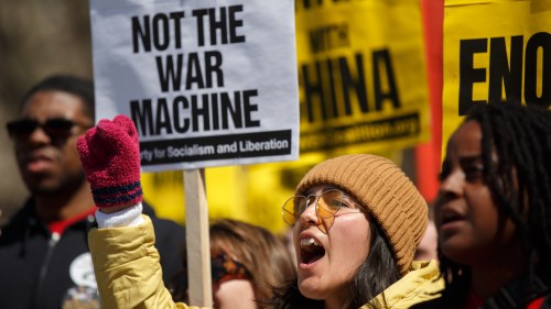 a protester speaks in front of a sign that says not the war machine