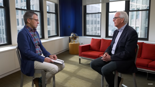 Ivo Daalder (R) and Ian Bremmer (L) sit facing each other on stools in front of a red couch and windows.