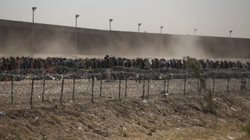Migrants line-up between a barbed-wire barrier and the border fence at the US-Mexico border