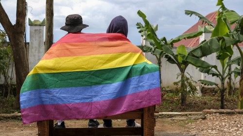 A gay Ugandan couple cover themselves with a pride flag as they pose for a photograph in Uganda