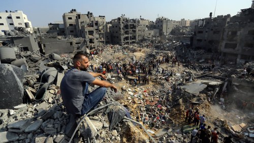 A man sits on the rubble as others wander among the debris of buildings that were targeted by Israeli airstrikes in Jabaliya refugee camp