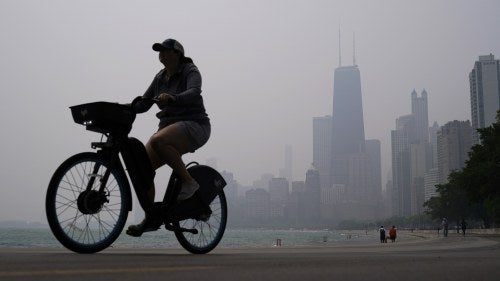 Woman bicycling against the Chicago skyline blanketed in haze from Canadian wildfires