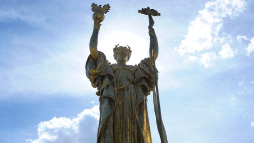 A tall gold statue with a blue sky in the background