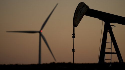 A pumpjack operates in the foreground while a wind turbine at the Buckeye Wind Energy wind farm rises in the distance