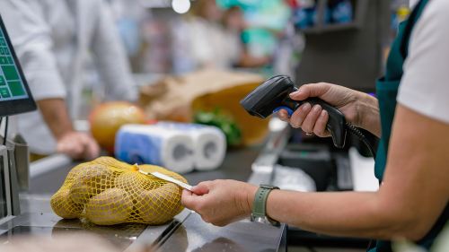 A grocery store cashier scans a bag of potatoes at the checkout counter.