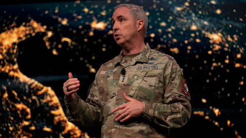 General Stephen N. Whiting speaks in front of a screen showing a close-up photo of Earth from space.