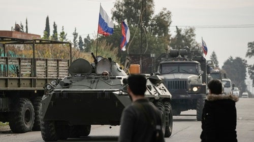  Syrian fighters watch Russian armoured vehicles driving past near the Hmeimim Air Base