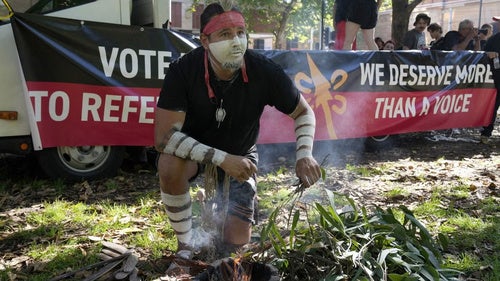 Aboriginal man Josh Sly of the Muggera Dancers prepares a fire for a smoking ceremony at the start of an Invasion Day rally in Sydney