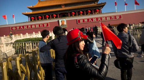 A woman holds a Chinese flag as she poses for a photo near Tiananmen Gate