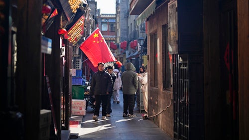 People walk past a Chinese flag in a commercial area in Beijing